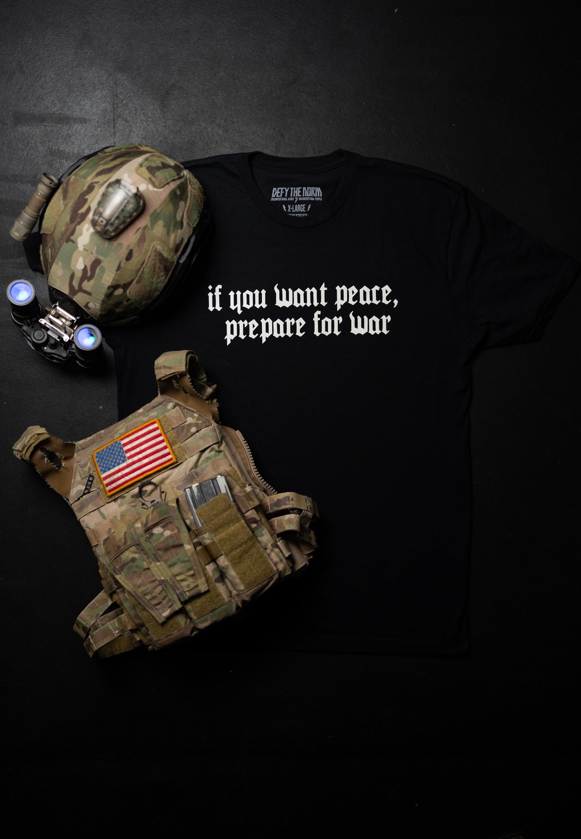 Black t-shirt with text, tactical vest, and helmet on a dark background